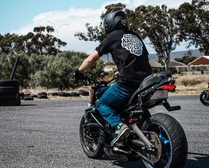 Person riding a motorcycle on a road with trees and buildings in the background